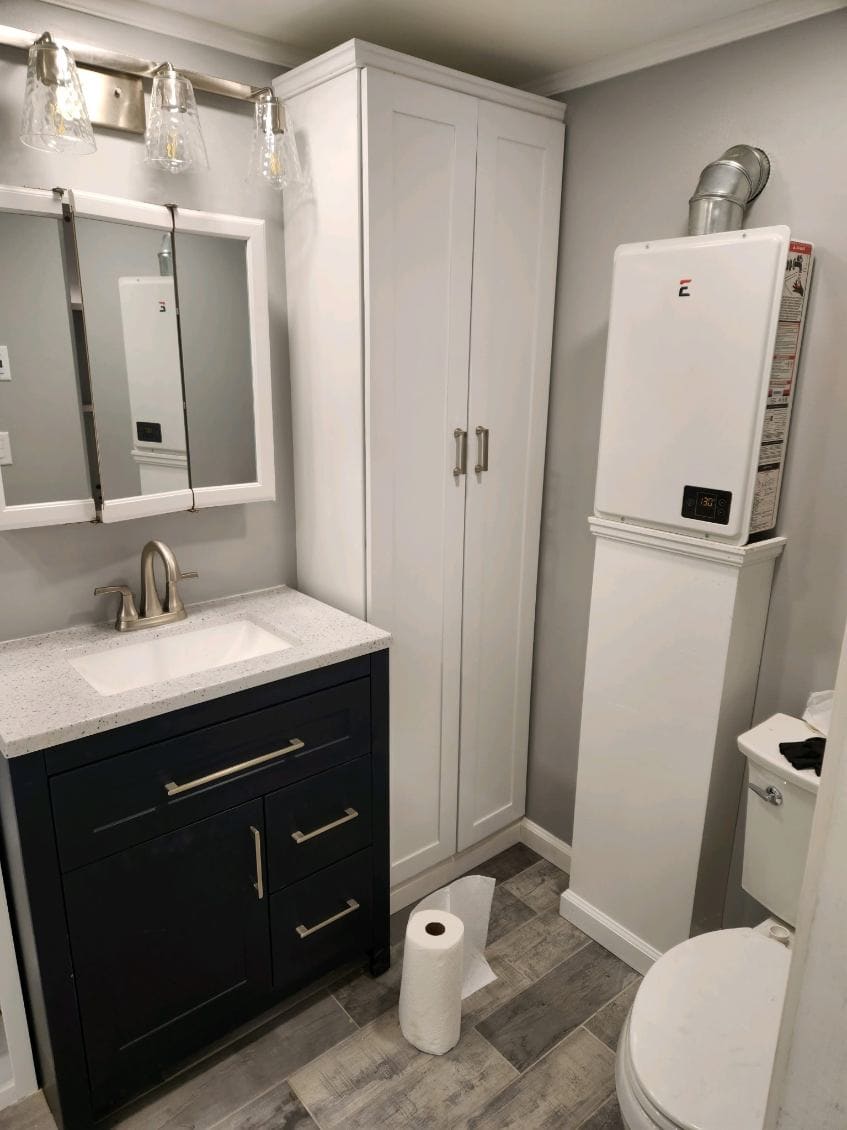 Remodeled bathroom with a navy shaker vanity, speckled quartz top, framed medicine cabinet, and a full-height white linen tower