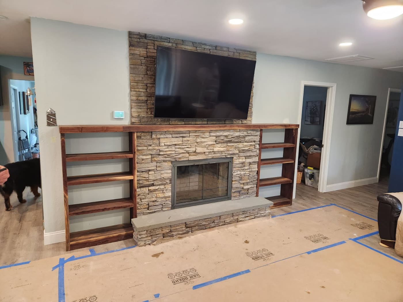 Stacked-stone fireplace surround with a walnut mantel and matching built-in walnut shelving, living room floor covered in protective board