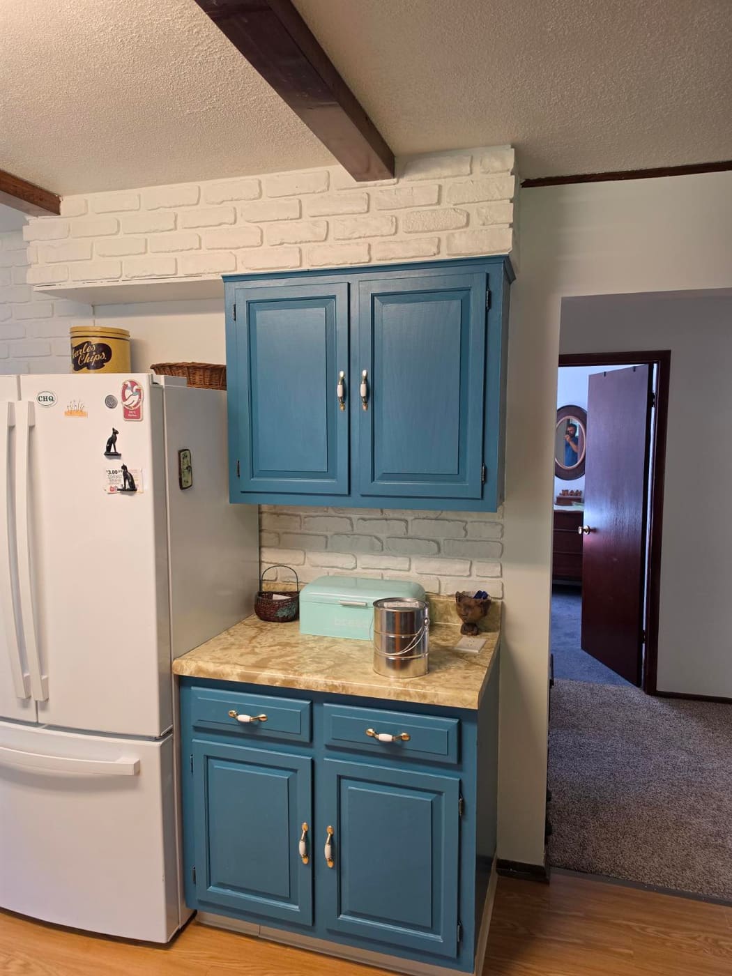 Interior brick painted bright white above blue cabinets, wrapping the soffit and the wall beside the refrigerator