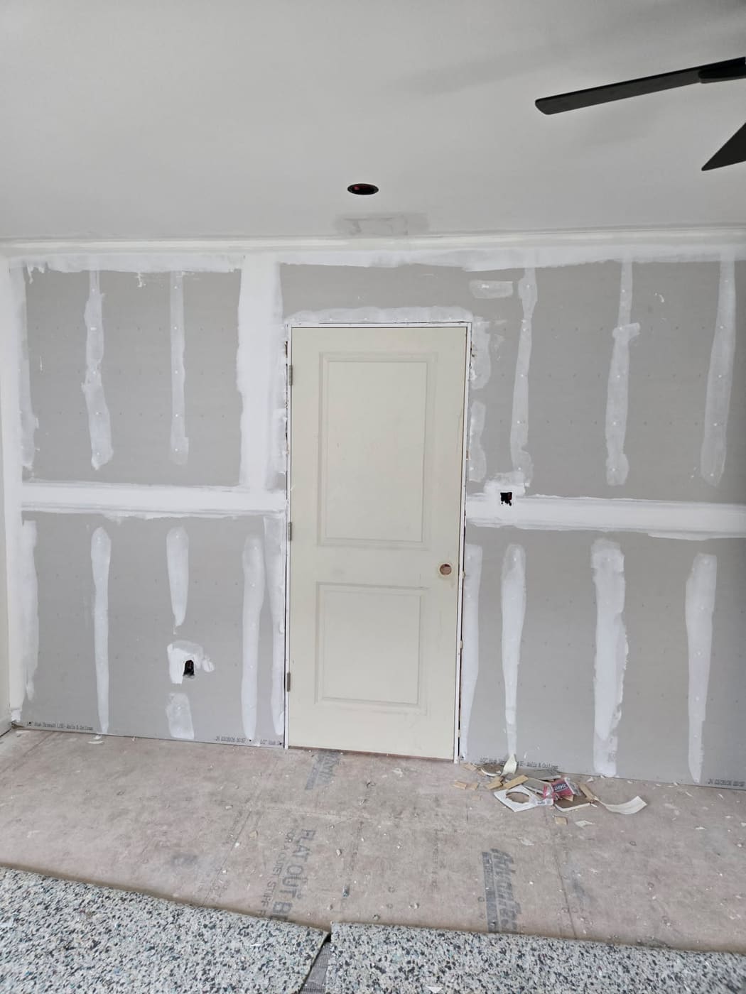 Drywall hung, taped, and mudded across a bedroom with a new six-panel door set and the floor papered
