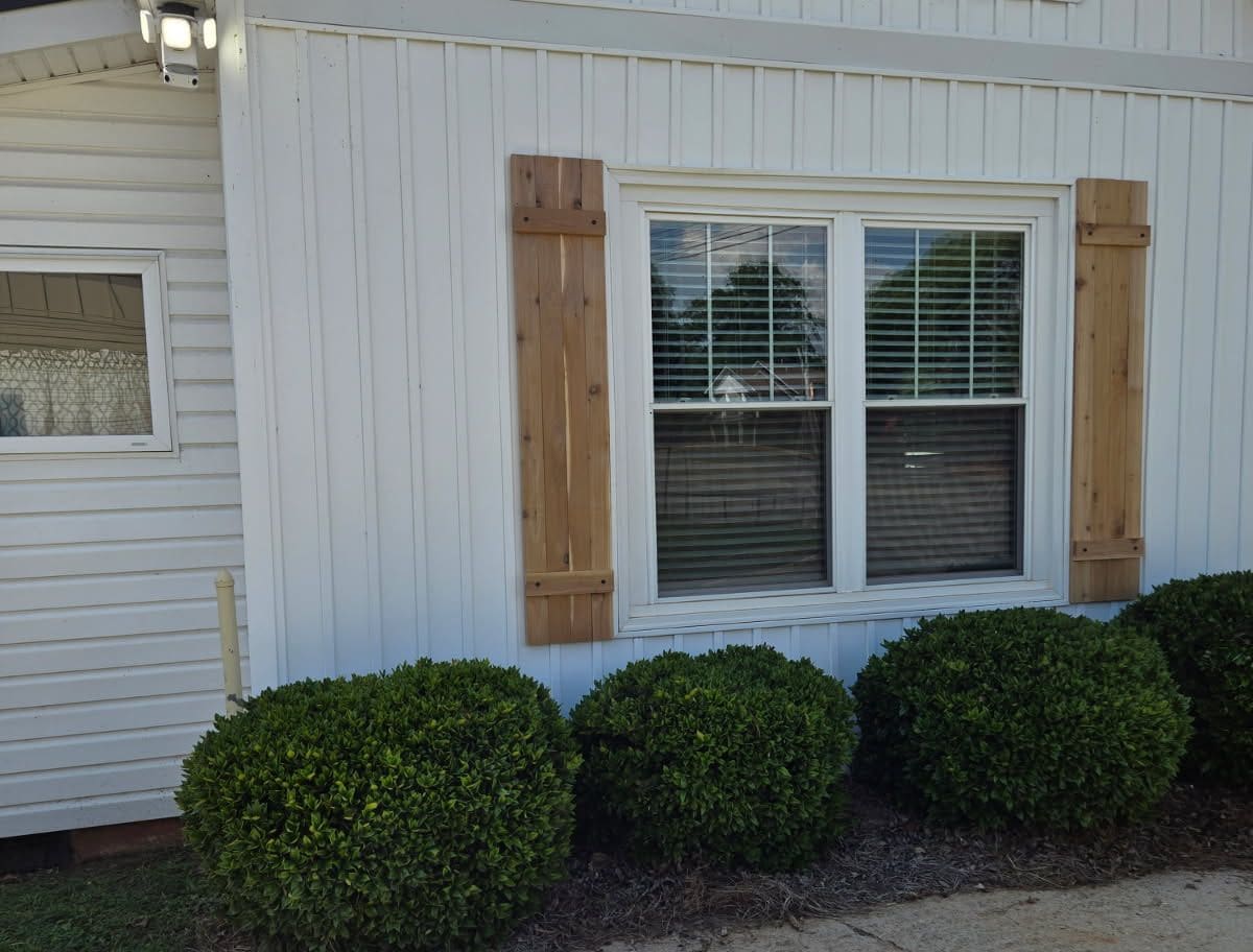 Custom red cedar board-and-batten shutters hung either side of a front window over white siding
