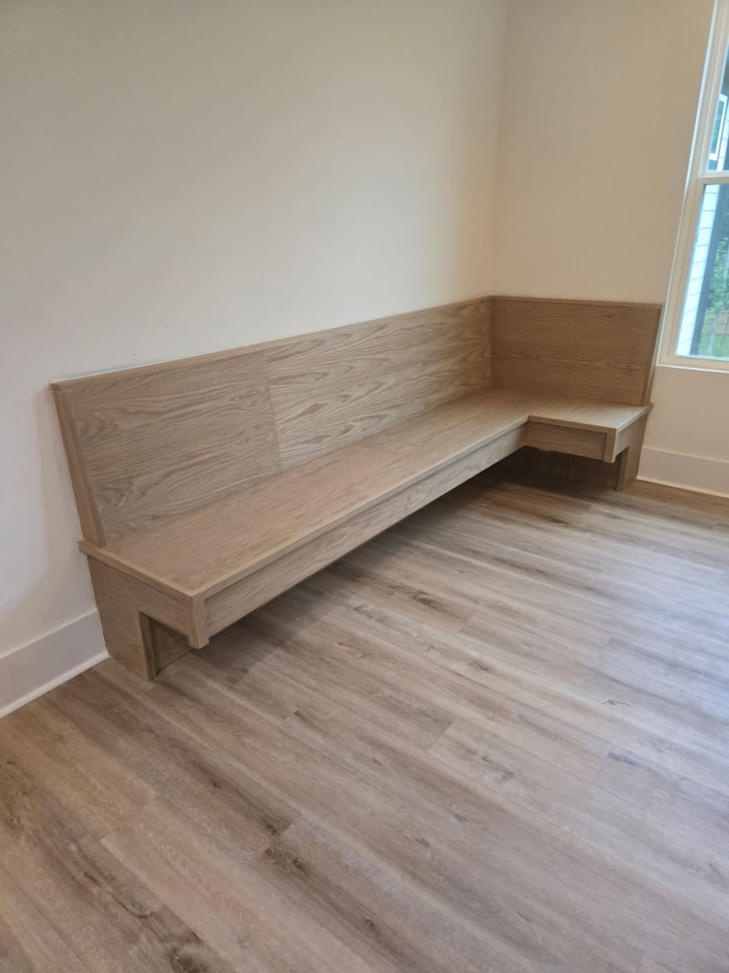 Custom white oak banquet bench built into a dining nook, wrapping two walls with a low back and a return under the window