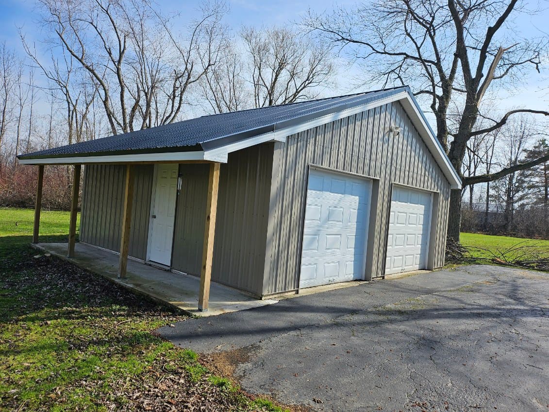 Detached two-car garage build finished in vertical steel siding with a standing-seam roof and a covered side porch