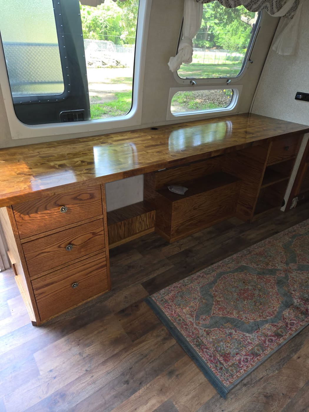 Modular red oak desk with a butcher block top, built into an Airstream camper over the wheel well with drawers and open shelving