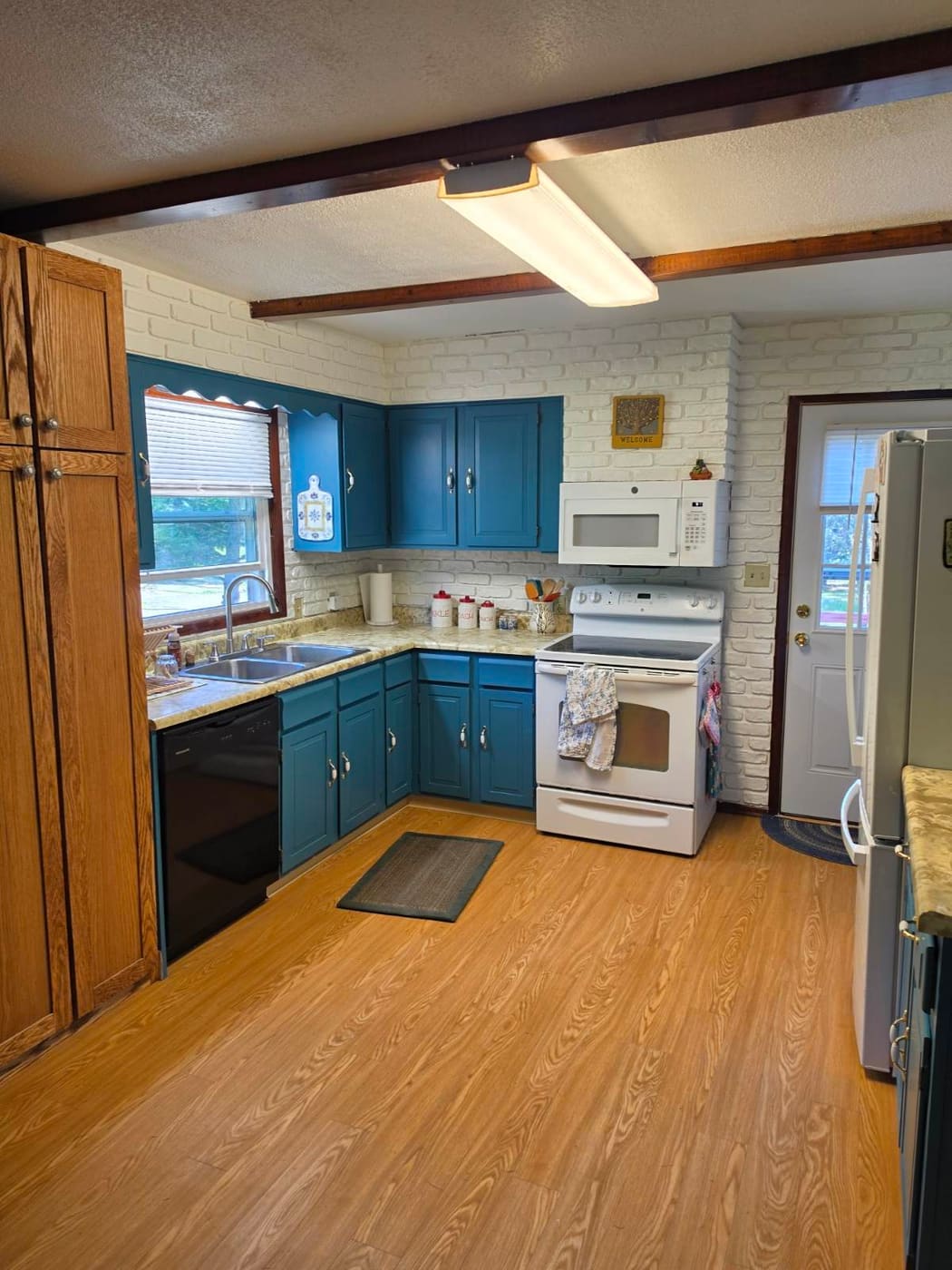 The kitchen from the doorway: painted brick and walls the length of the room, blue cabinets, and the custom red oak pantry standing at the near corner