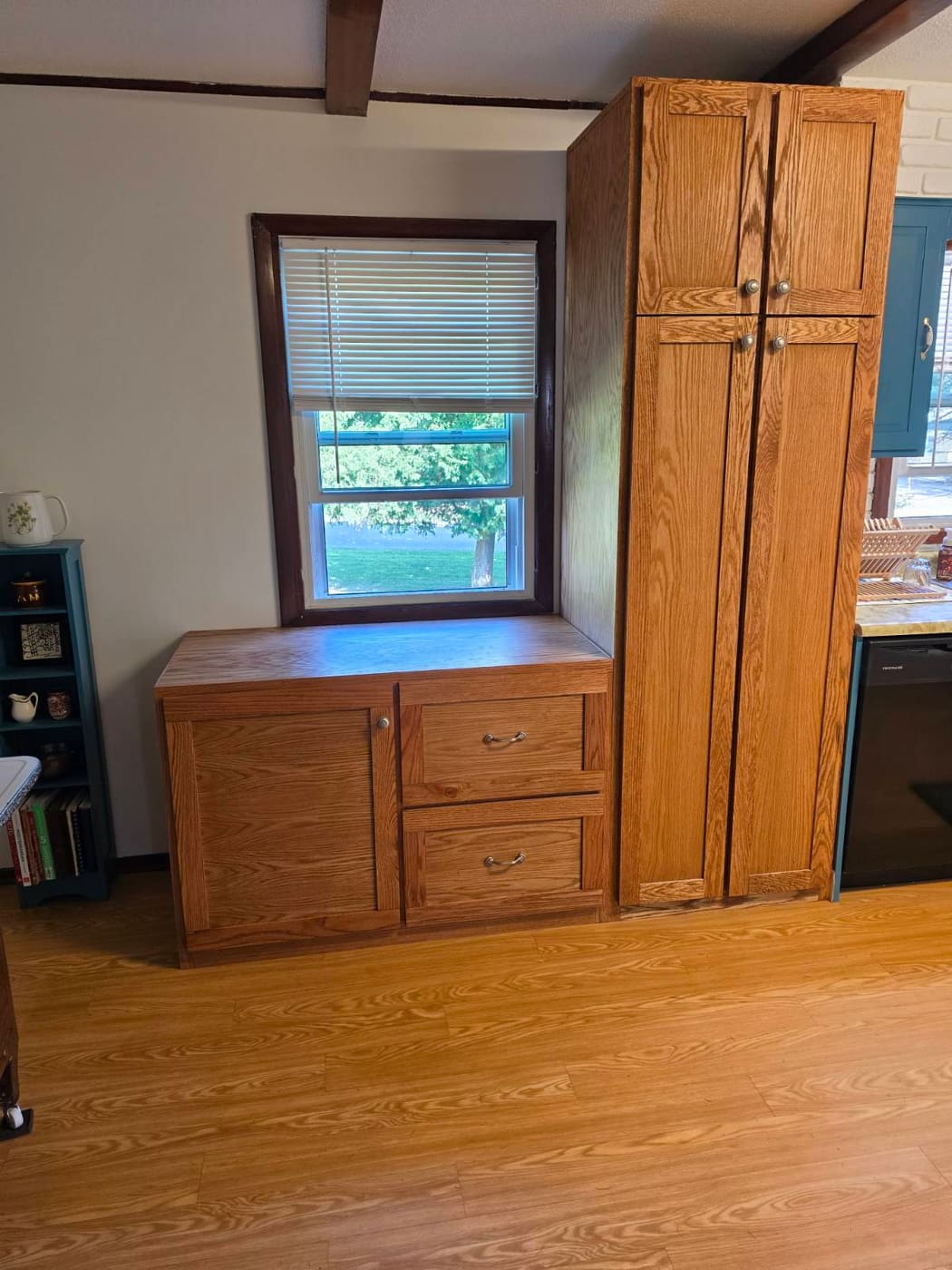 Two custom red oak cabinets built for the same kitchen, a drawer base under the window and a full-height pantry beside it, grain and stain matched